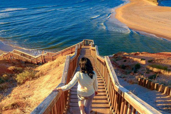 Woman walking down steep wooden steps towards a beach in the late afternoon