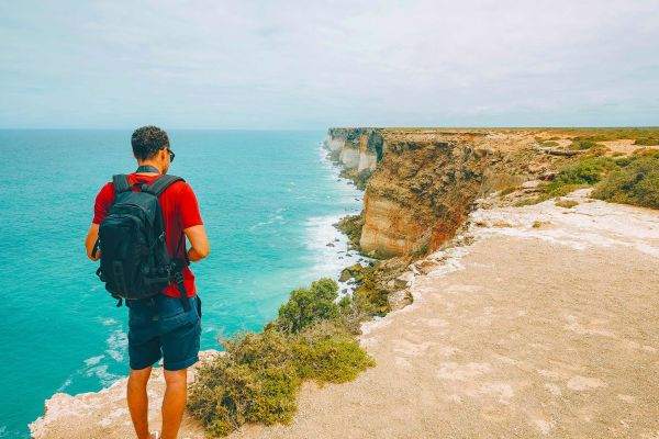 Man standing on the edge of a cliff looking down at the ocean
