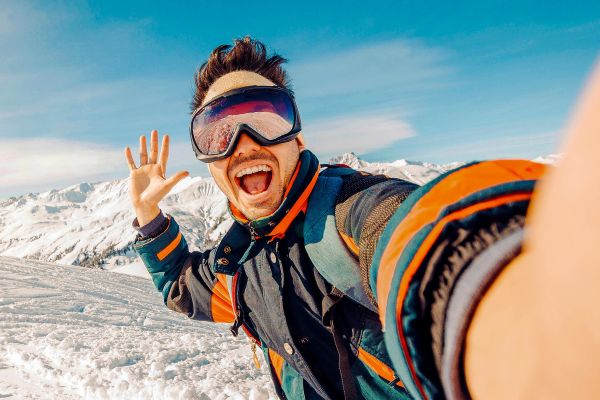 Man taking a selfie in snow gear at the top of a mountain