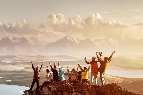 Group of people cheering at the top of a mountain at sunset