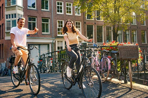 man and woman laughing and riding bikes over canal in amsterdam