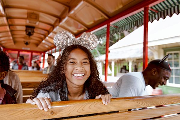 young girl with mickey ears smiling while sitting in a small train