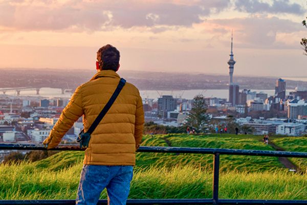 person in yellow puffer jacket standing on hill looking over auckland