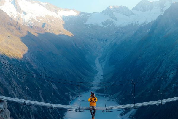 Man in yellow jacket sitting on a suspension bridge over a lake in Olpererhutte,