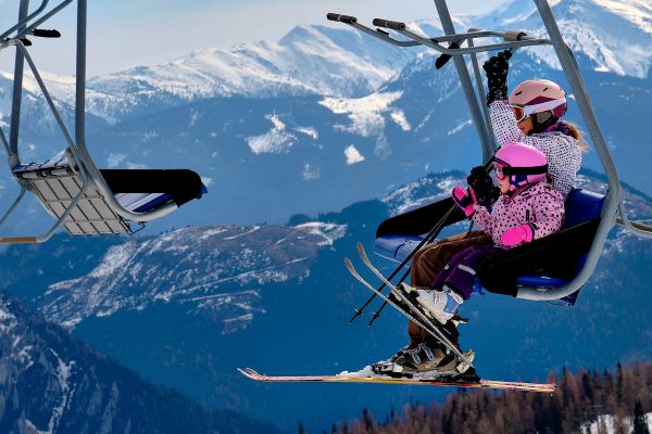 Mother and daughter taking chair ski lift up the mountain during skiing vacation 
