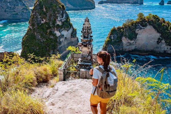 Backpacker walking towards monument on a cliff facing the ocean