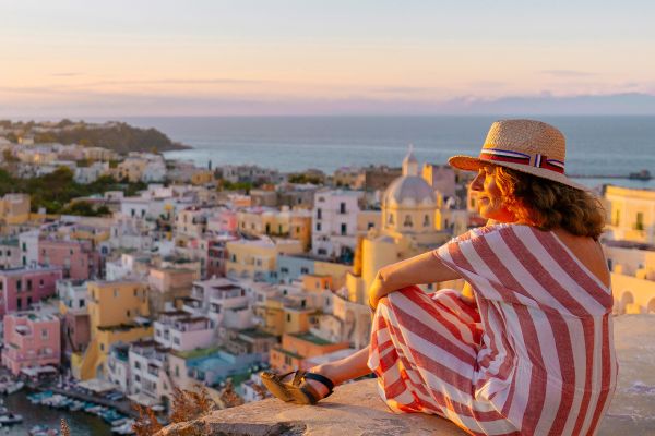 Woman in a stripped dress sitting on a wall overlooking a coastal city at sunset