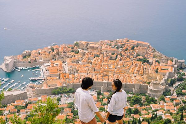 Couple holding hands on a cliff looking down at Dubrovnik