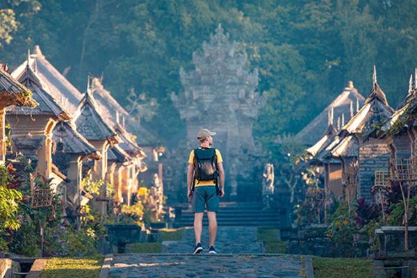 man walking away from camera down a path lined with small huts in bali