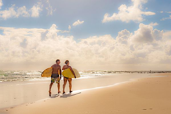 Walking along beach holding surf boards