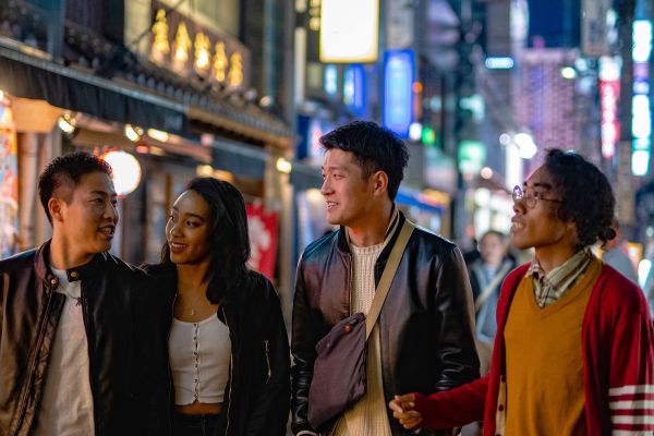 Four young adults walking down a neon-lit street at night