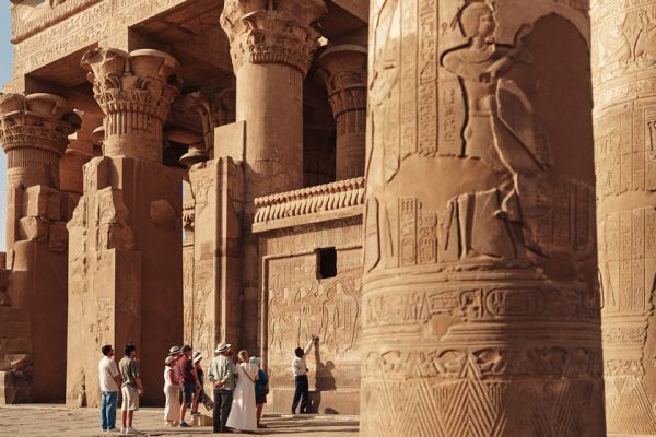 Tour group inspecting large Egyptian hieroglyphs on a sunny day