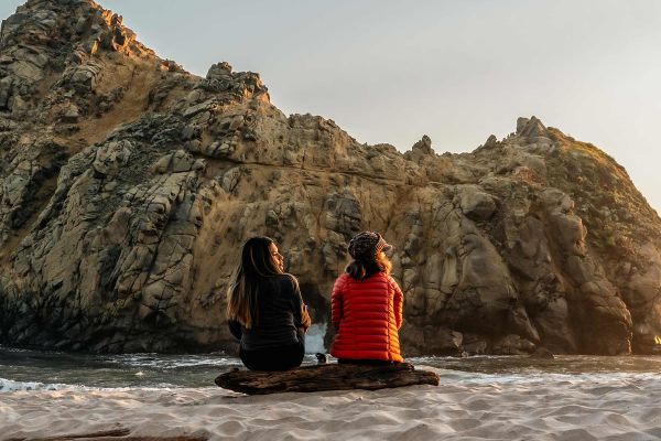 Two girls sitting on a beach looking at the ocean
