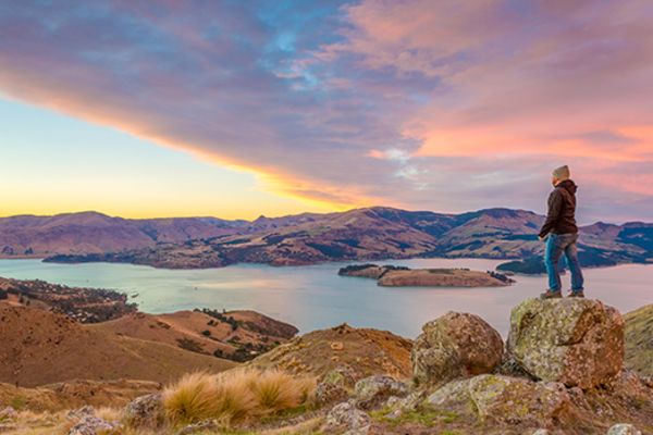 man standing on rock on mountain overlooking lake in christchurch