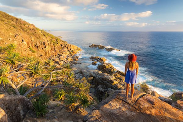 Woman in a purple dress and red hat looking out at the ocean from rocks