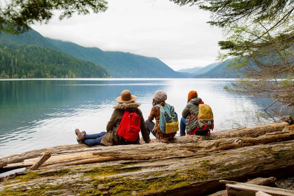 Three people sitting on log looking out at lake