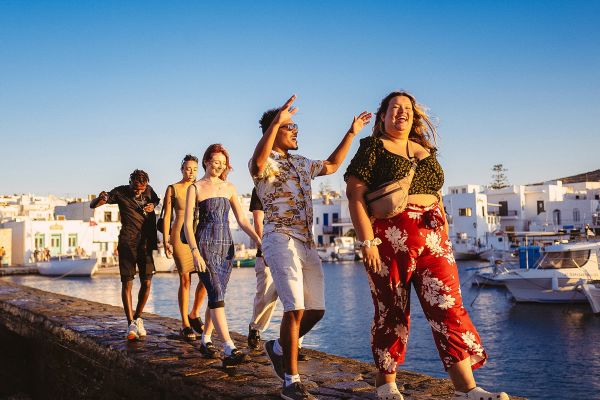 Friends walking along a thin, rocky walkway in a harbour