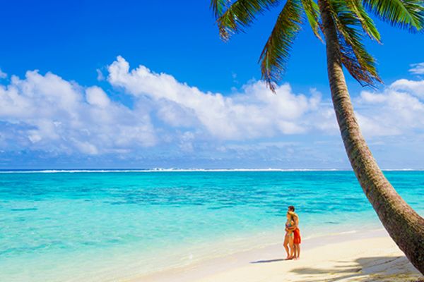 woman and child standing on beach under a tree in cook islands