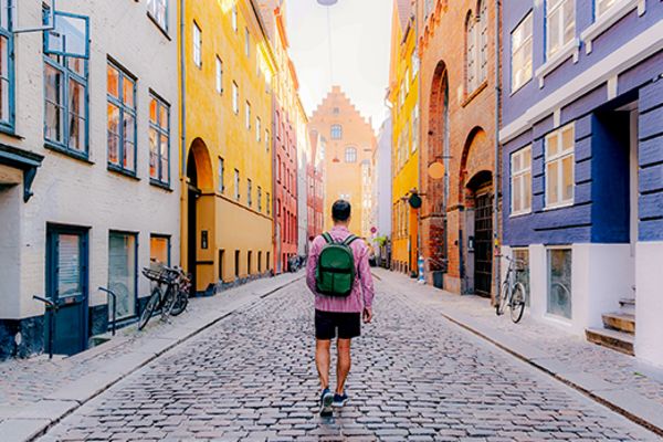 Man walking down a brick street past brightly coloured, tightly packed buildings