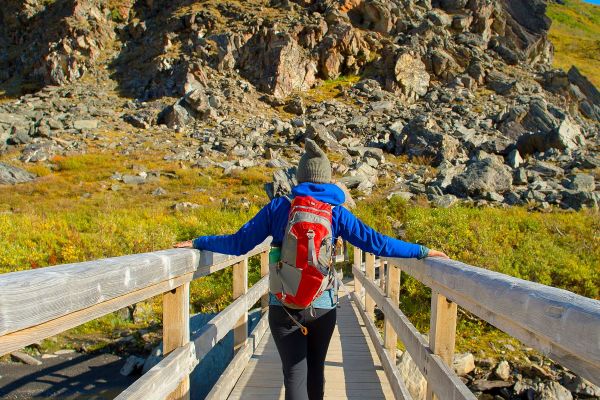 Person in light hiking gear walking along a wooden bridge towards a rocky hill