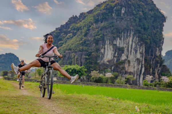 Woman excitedly riding a bike down a dirt path with large, forested mountain in the background