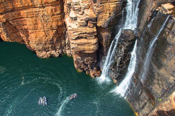 Aerial shot of a boat crusing along the cliffs with a waterfall