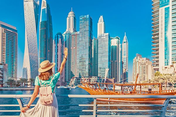 Woman waving to a ship sailing past with the city of Dubai across the water in the background