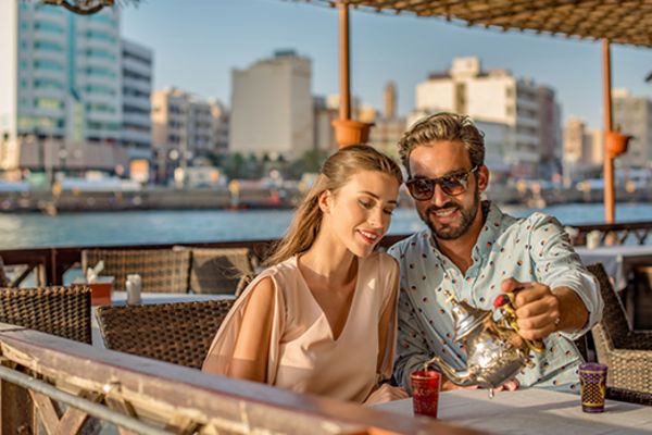 Couple sharing tea in a restaurant with the city of Dubai in the background