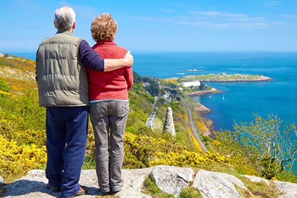 Two old people standing on a cliff looking out at the ocean
