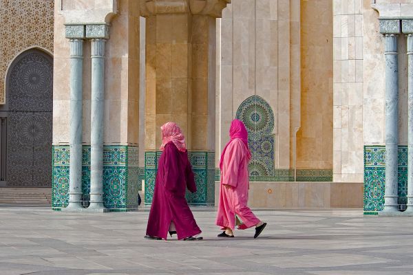 Women wearing pink and purple traditional middle eastern clothing walking past pillars