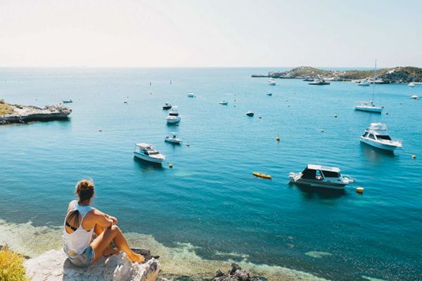 Lady sitting on hill overlooking water with boats