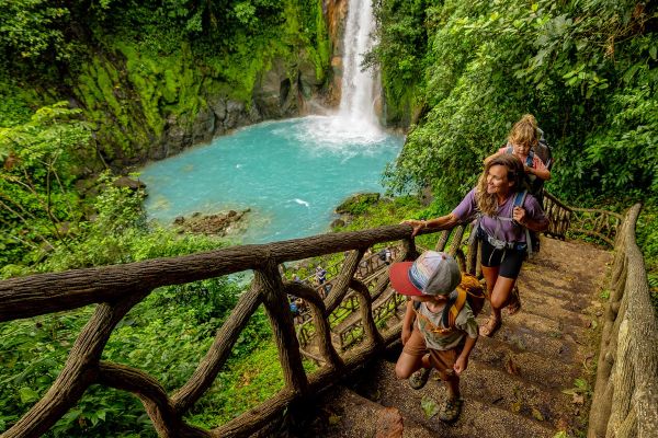 Family of three walking up a staircase built into a rainforest with a waterfall in the background