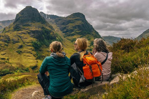 Three women sitting on the ground looking out at rolling hills