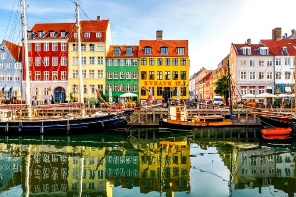 Colourful waterfront buildings and moored boats lining Copenhagen's Nyhavn harbour reflected in calm canal waters on a sunny day
