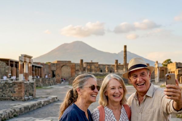 Three travellers smiling for a selfie among the ancient ruins of Pompeii with Mount Vesuvius rising in the background at sunset