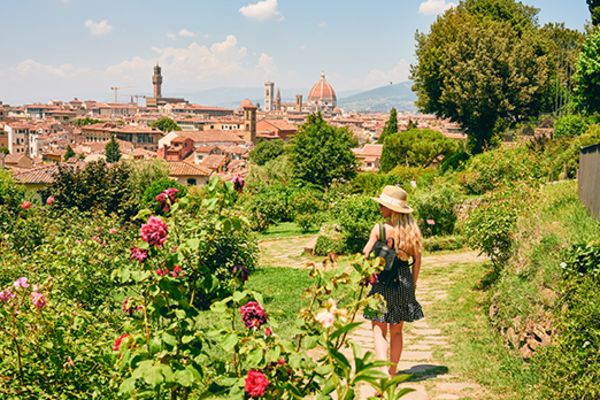 Woman walking through a bright green garden with the city of Florence in the background