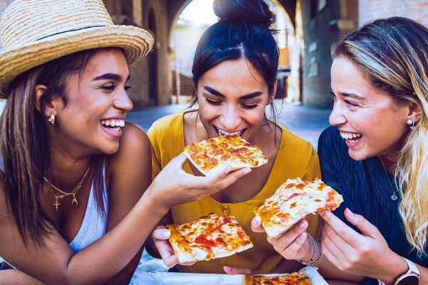 Three friends smiling, and eating pizza