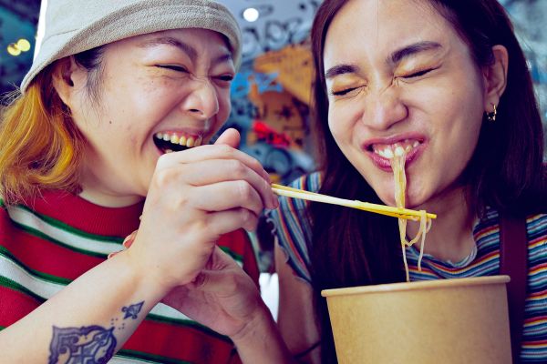 Couple laughing sharing a bowl of noodles