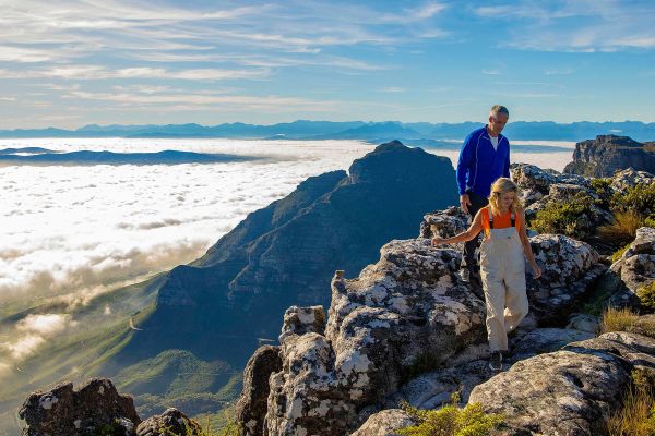 Top people at the top of a tall mountain looking down at the clouds