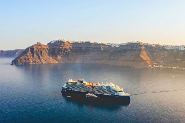 Wide shot of a cruise ship sailing past steep rocky cliffs