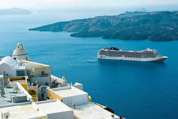 Cruise ship on a clear ocean, framed by bright white Greek buildings
