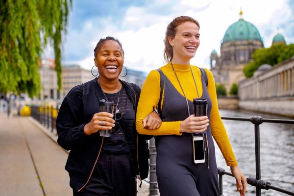 Cheerful friends walking on footpath by river in city