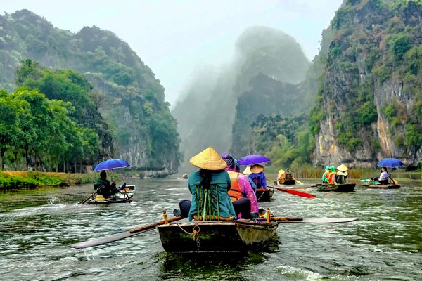 Several rowboats heading towards tall, tree-covered mountains