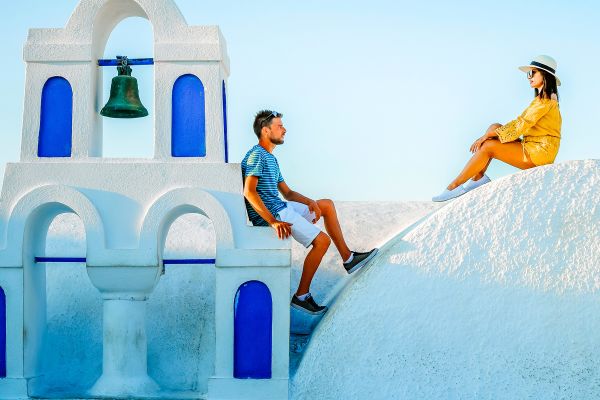 Man and woman sitting on the roof of a white stone building in Greece