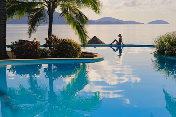 Woman relaxing on the edge of a pool looking at the ocean
