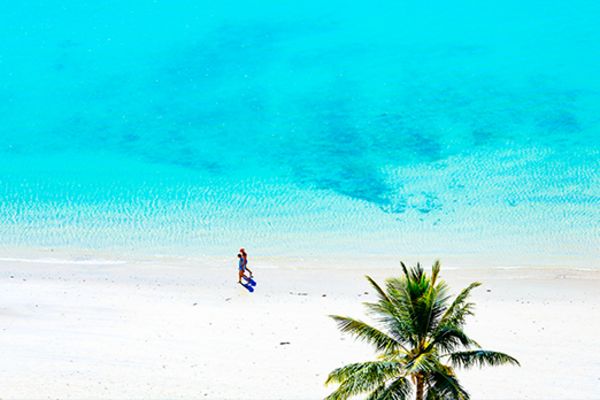 Wide shot of a couple walking along a beach next to a bright blue ocean