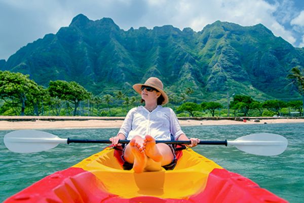 Person in a red and yellow canoe holding a paddle, relaxing with a mountain in the background