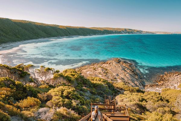 Wide shot of a woman standing on a long wooden staircase leading to the ocean