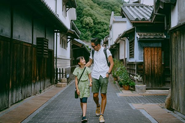 Parent and child walking down a street in Japan passed buildings made of weathered wood