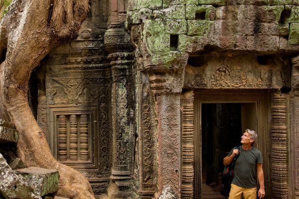 Man walking through an ancient ruin overgrown with trees and moss